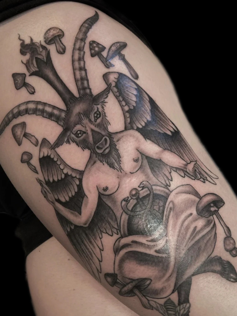Black and grey Baphomet tattoo surrounded by mushrooms, on the thigh