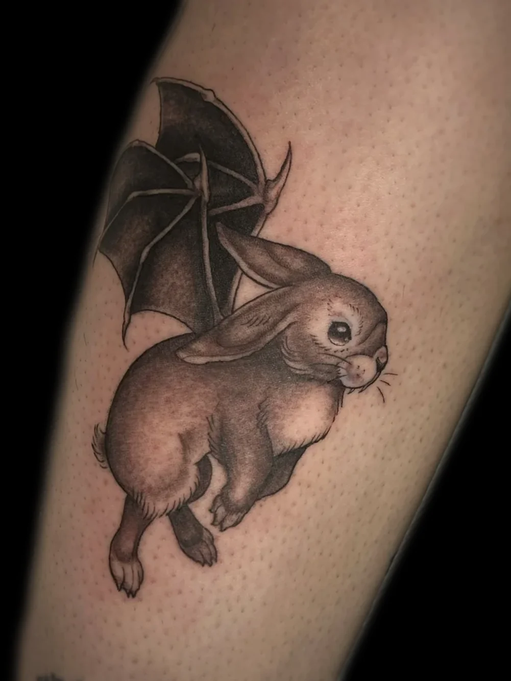 Bunny with bat wings tattoo, black and grey, on the lower leg