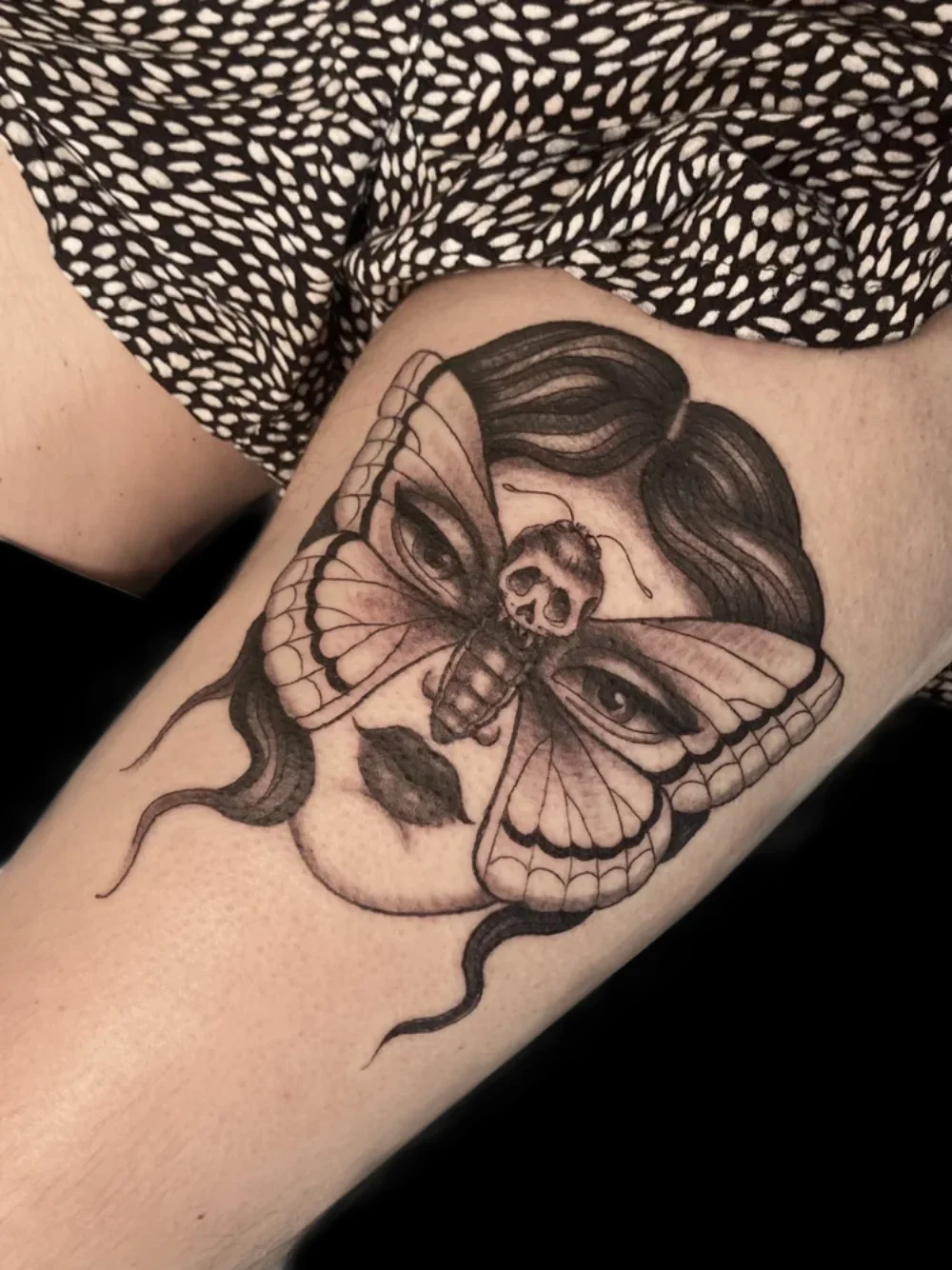 Death's-head moth forming a mask over a woman's face, tattoo on the thigh